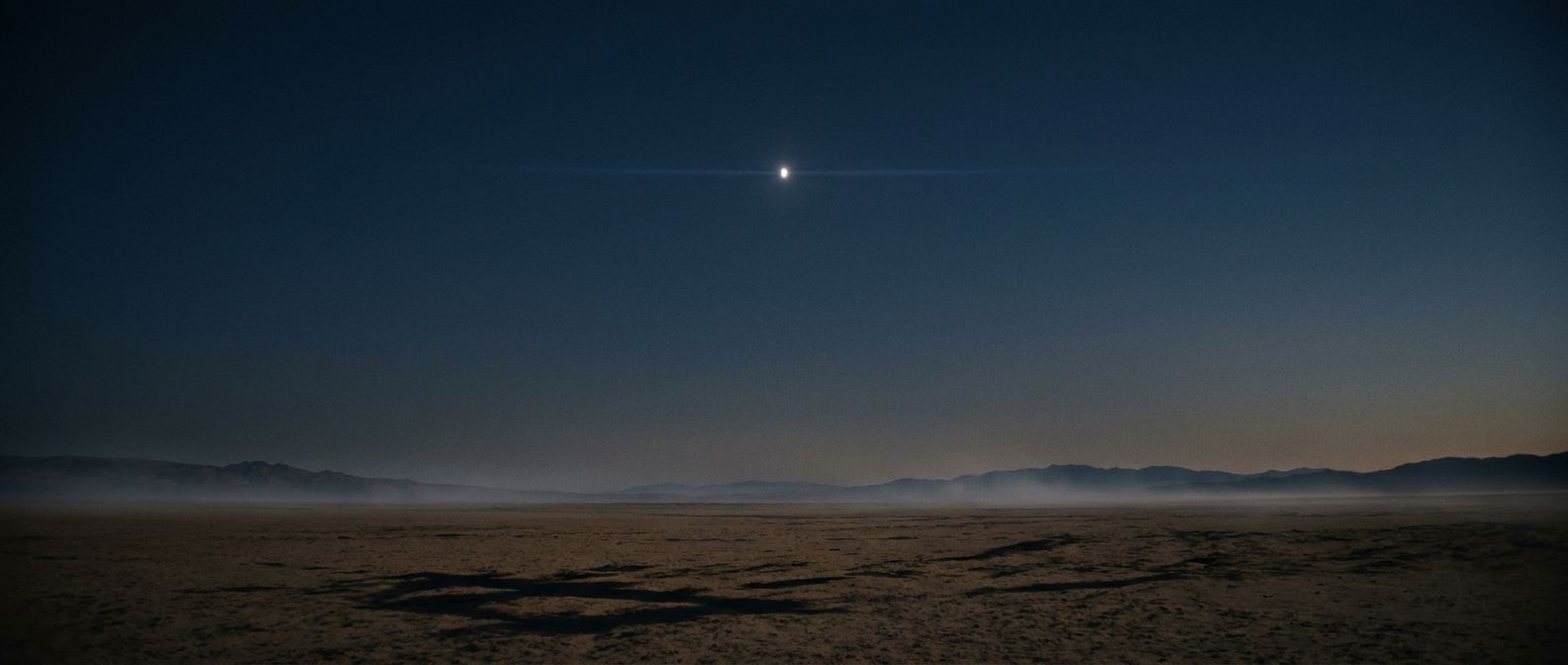 A dark savanna plain at dusk with a burning amber horizon and a single bright star